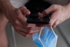 Hände, die ein Handy und eine Maske halten