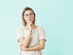 Eine Frau mit Brille und der Hand am Kinn blickt nachdenklich nach oben