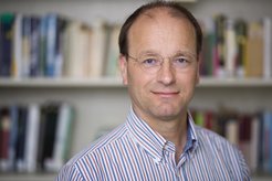 Das abgebildete Foto ist ein Portrait. Ulman Lindenberger, Direktor des Forschungsbereichs Entwicklungspsychologie und Vizepräsident der Geistes-, Sozial- und Humanwissenschaftlichen Sektion der Max-Planck-Gesellschaft, befindet sich im Vordergrund und ist bis Brusthöhe abgebildet. Er lächelt in die Kamera. Im Hintergrund ist ein unscharfes Bücherregal zu erkennen.