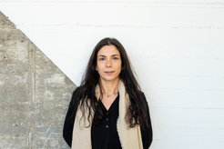 The photo shows Nour Tawil (feminine) in portrait in front of a concrete-like wall, diagonally divided and painted white in the upper right half.