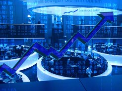 Bild in Blautönen mit Blick auf die vielen Bildschirme an der Frankfurter Börse und einem nach oben zeigenden Zickzack-Pfeil im Vordergrund.