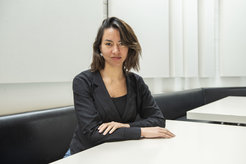 The picture shows Yayouk (female) in portrait sitting at a table. She is wearing a black blazer and her short brown hair is loose.