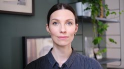 Auf dem Bild ist Laurel Raffington (weiblich) im Porträt zu sehen. Sie trägt ihr braunes Haar in einem Zopf und trägt ein dunkelblaues Jeanshemd. Im Hintergrund ist eine dunkelgrüne Wand mit Bildern zu sehen.