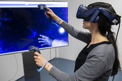 Eine Person nutzt ein VR-Headset und zwei Controller, während sie vor einem großen Bildschirm steht, der eine Weltraumszene zeigt.