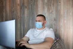 Man with mask sits at computer