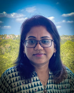 The picture shows a blue sky with clouds, green trees and the portrait of Kavitha Ranganathan in the foreground.