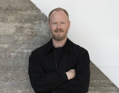 The photo shows the portrait of Dirk Wulff in front of a gray and white wall.