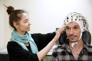 Dieses Bild zeigt eine Forschungsassistentin und neben ihr sitzt ein Proband mit einer EEG-Kappe.