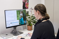 Dieses Bild zeigt eine Forschungsassistentin bei der Arbeit, die an einem Tisch vor einem Computer sitzt. Auf dem Bildschirm ist ein Video mit einer Mutter und ihrem Kind in einem Garten zu sehen sowie ein Programm zur Verhaltenskodierung.