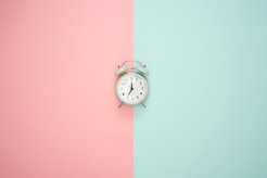 The background is pink on the left and mint green on the right, in front of it is an alarm clock