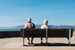 Zwei ältere Menschen sitzen auf einer Bank und schauen auf ein Bergpanorama