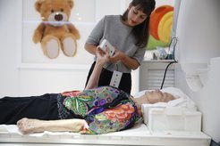 A test person lies on the MRI table, next to her is a research assistant